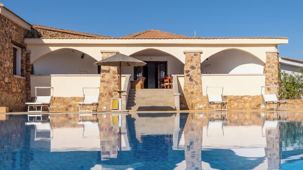 A poolside area with a clear view of a building with stone pillars and a tiled roof. - Chic Villa Antonina Num2179 (Golfo Aranci)