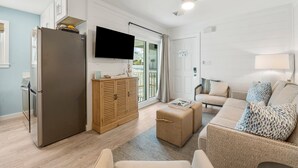Ein modernes Wohnzimmer mit einem großen Flachbildfernseher, einer integrierten Holzeinrichtung, einem beigen Sofa mit gemusterten Kissen und einem kleinen Hocker.
