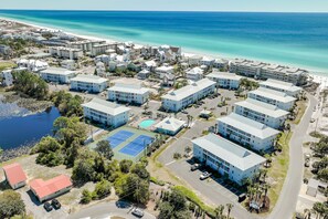 An aerial view of a coastal hotel complex with multiple buildings, a tennis court, and a beach in the background.