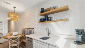Eine moderne Küche mit einer weißen Arbeitsplatte, einer eingebauten Spüle, einer Kaffeemaschine und Holzregalen über der Arbeitsfläche.