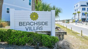 Schild für Beachside Villas, mit einem gelben Blütenlogo, umgeben von Grünpflanzen und Palmen.