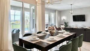 Un comedor con una mesa grande dispuesta para cuatro, una araña y vistas al exterior a través de puertas correderas amplias.