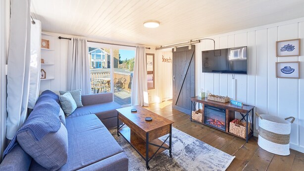 Un salon confortable avec un canapé, une table basse et un téléviseur. Une porte coulissante donne accès à un balcon aménagé avec du mobilier d’extérieur.