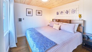Une chambre avec un plafond en bois, un lit avec une literie à motifs, une table de chevet et des œuvres d’art accrochées au mur.