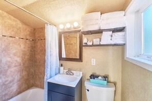 A bathroom with a bathtub, a sink, a toilet, a mirror, and a shelf with towels. - Romantic, Walk to town & beach (Akari#3) (Long Beach)