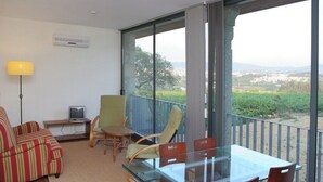 Ein Balkon mit Glastisch und Stühlen, einer Couch, einem Fernseher und einer Lampe.
