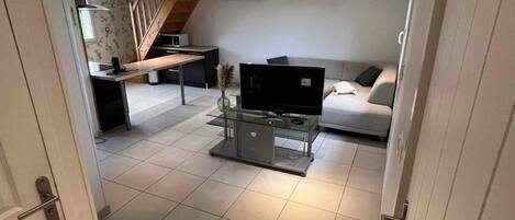 A modern living room with a sofa, a glass coffee table, and a TV. There is a staircase leading to another level.
