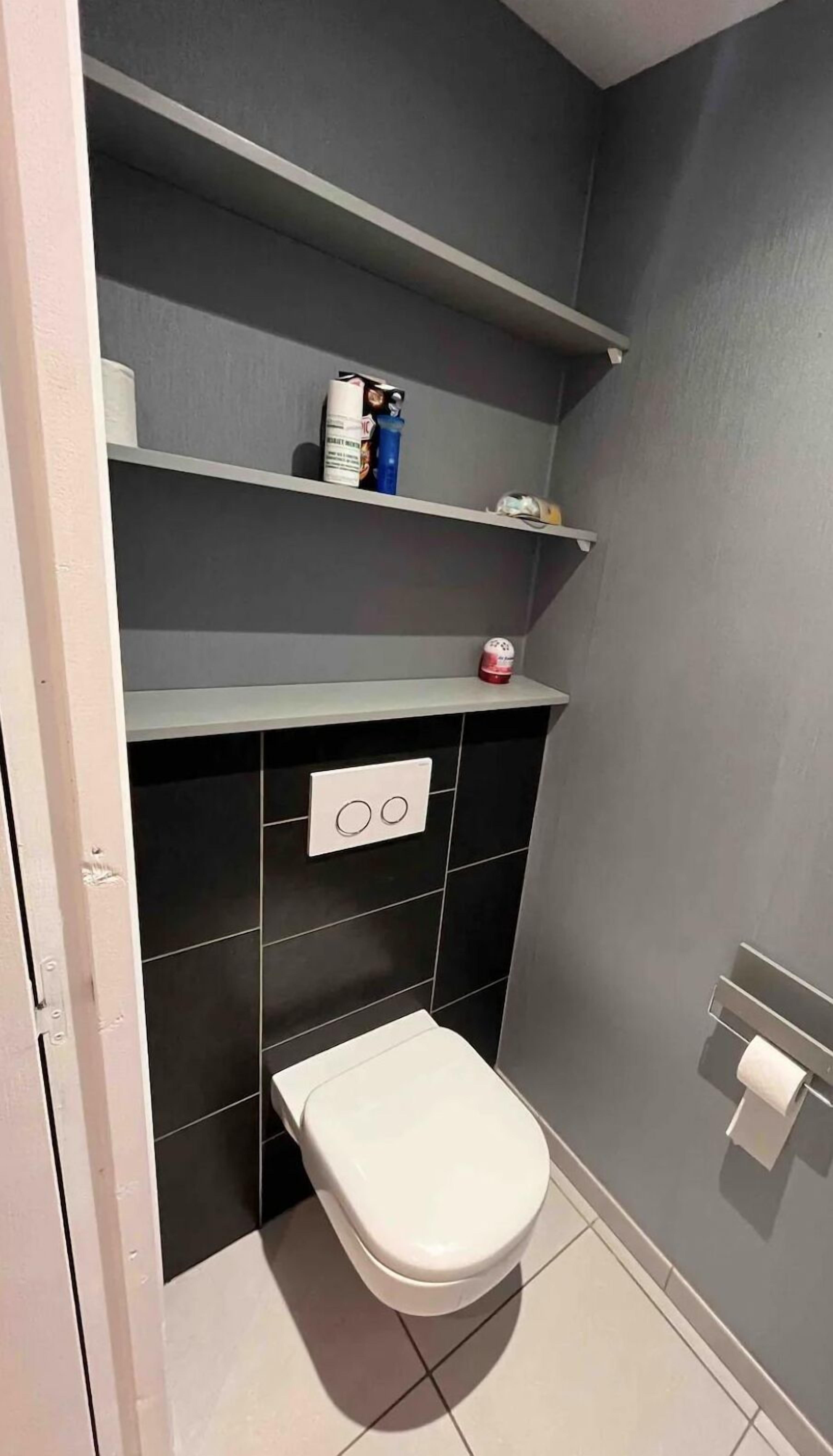 A small bathroom with a toilet, a shelf with toiletries, and a wall-mounted toilet paper holder.