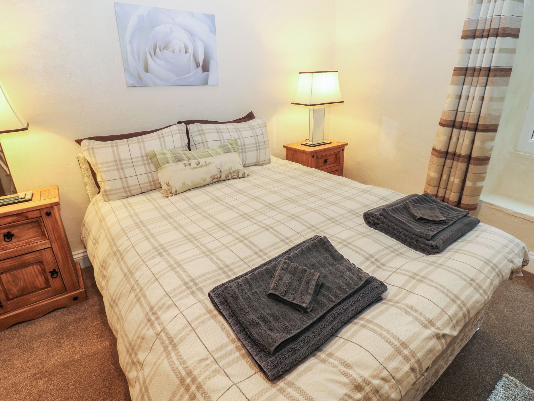 Una cama bien hecha con ropa de cama escocesa, dos lámparas de noche, una mesita de madera y un cuadro colgado en la pared.