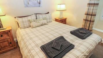 A neatly made bed with plaid bedding, two bedside lamps, a wooden nightstand, and a wall-mounted picture.