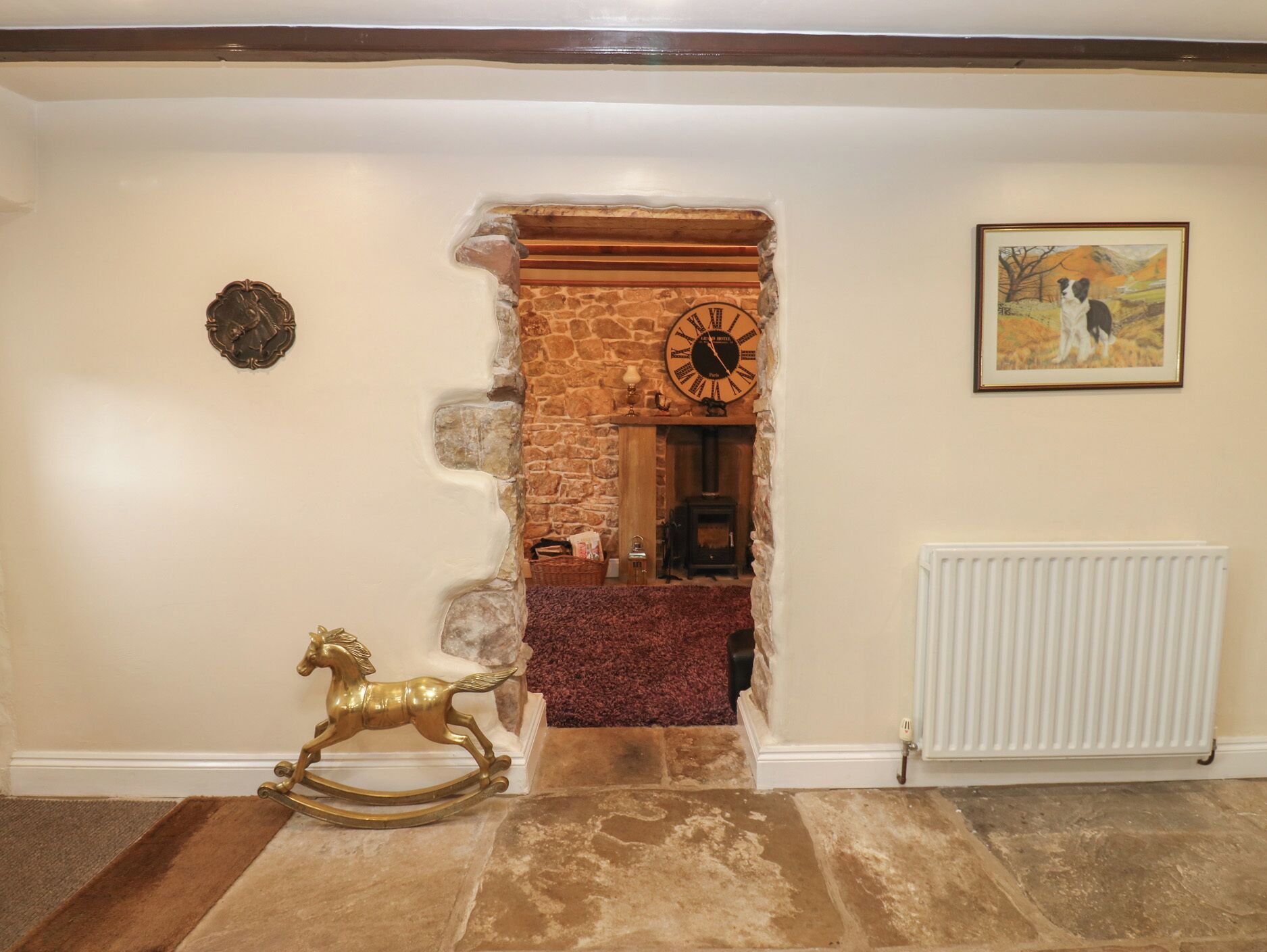 A hallway with a stone fireplace, a clock, a framed picture, and a brass rocking horse.