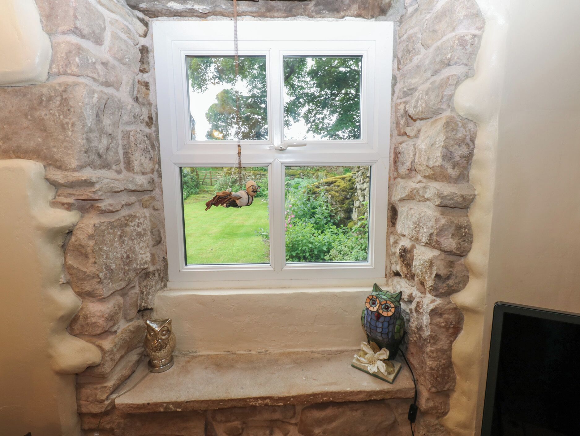 A stone-framed window with a view of greenery and a hanging ornament.