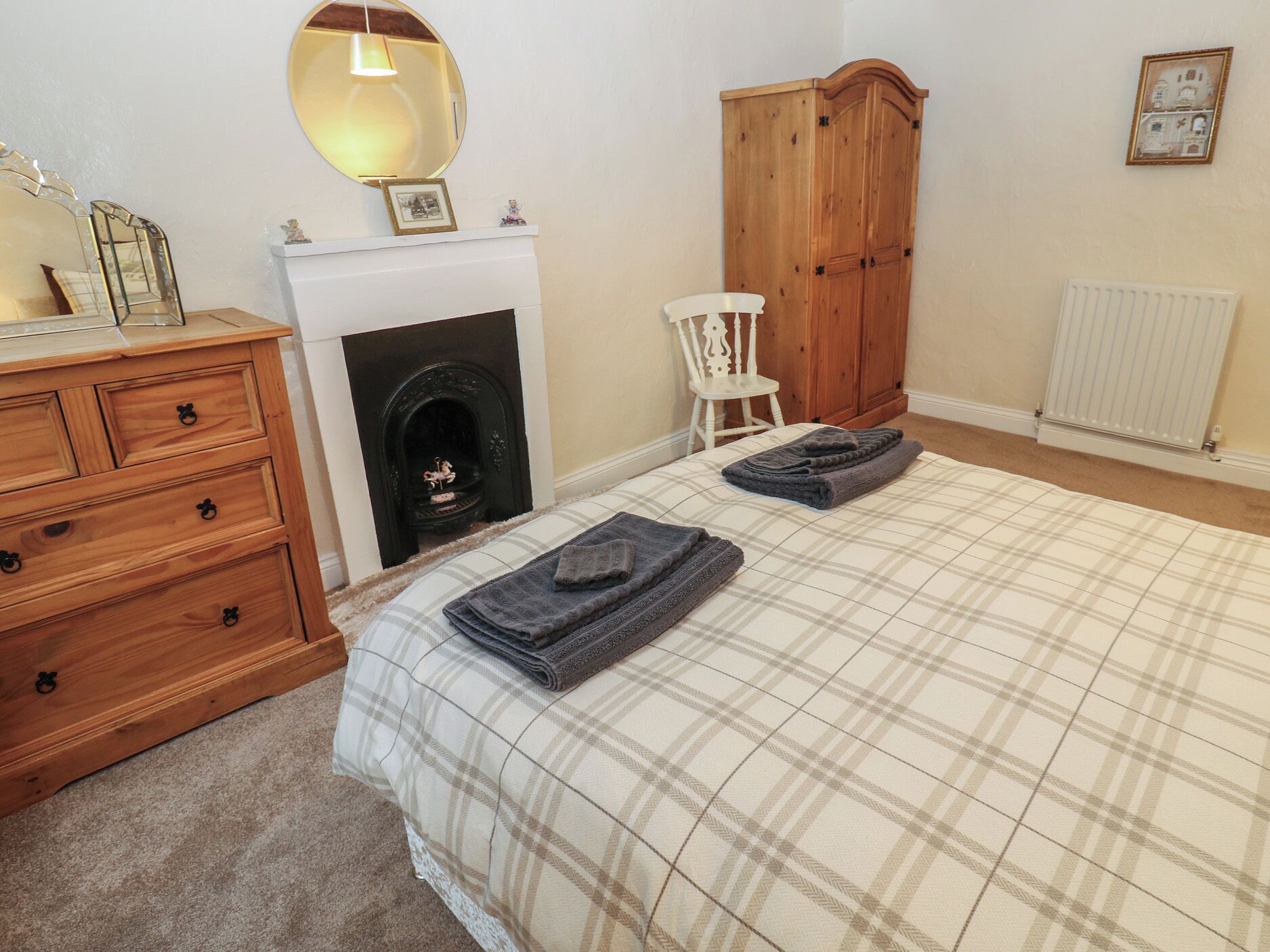 A bedroom with a bed, a wooden dresser, a wardrobe, a fireplace, a chair, and a radiator.