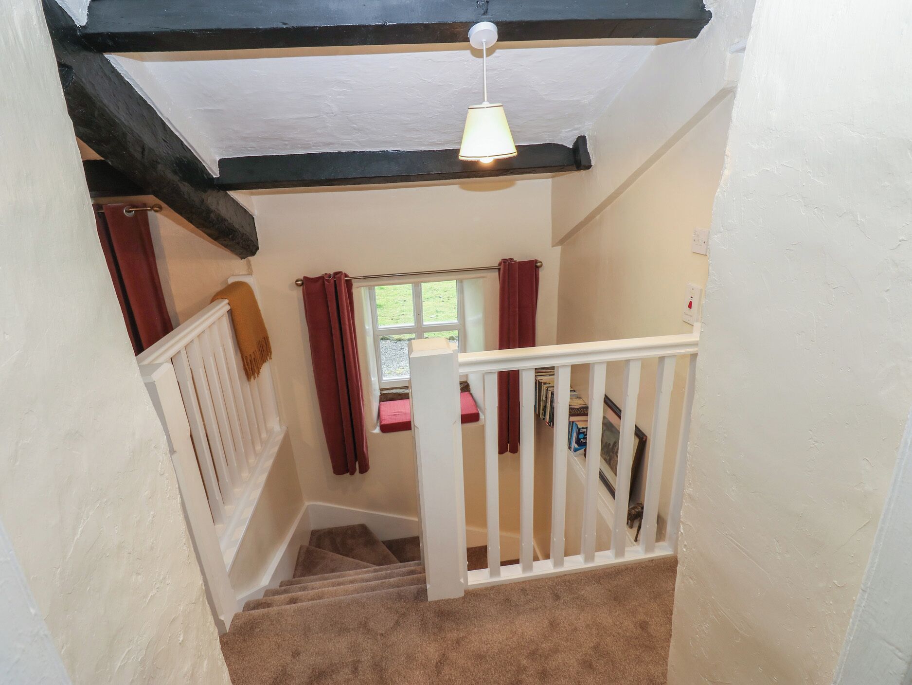 A staircase with a white railing, a red curtain, and a window with a view of the outside.
