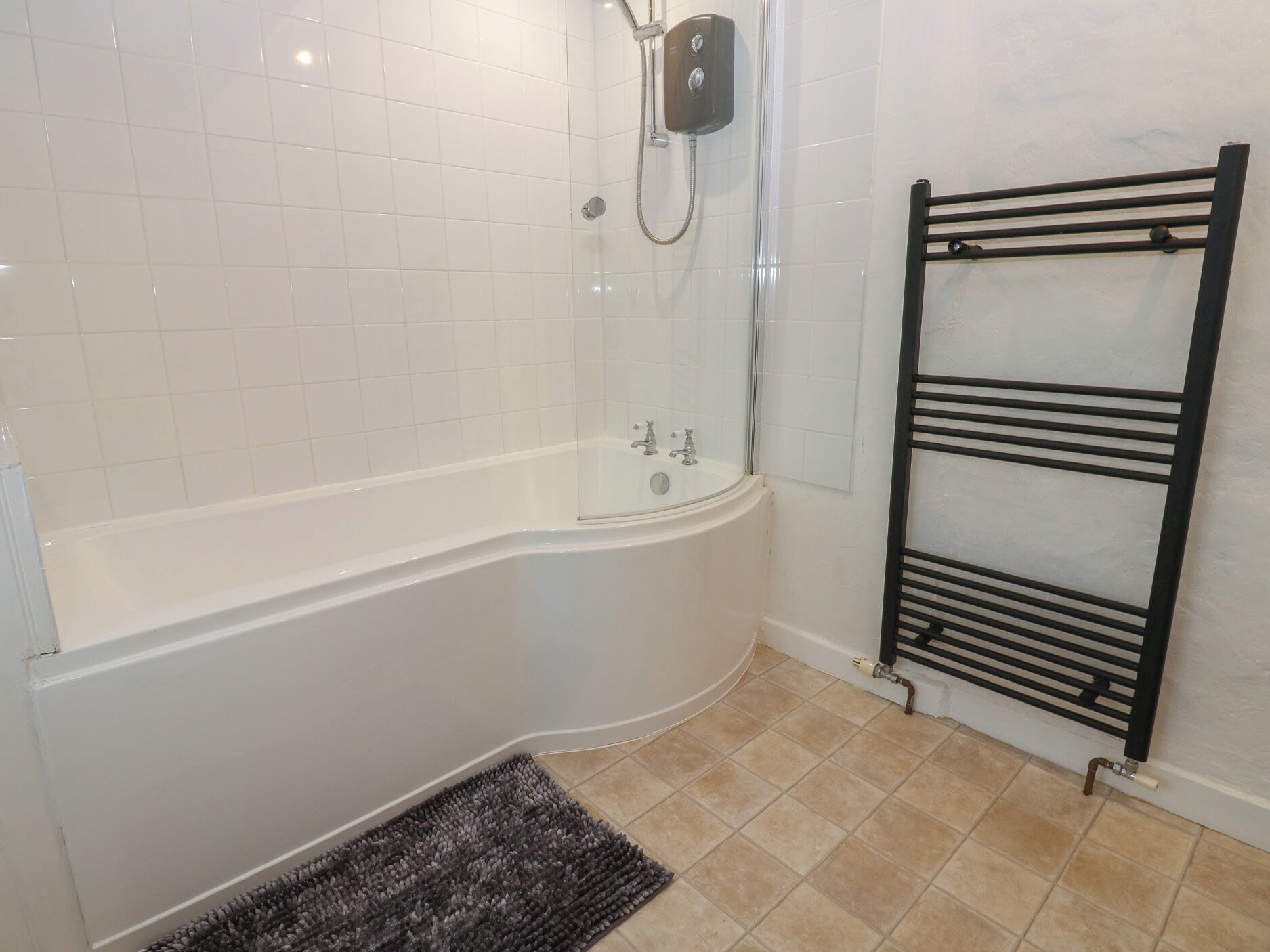 A bathroom with a white bathtub, a glass-enclosed shower, and a black towel rack.