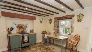 A kitchen with a stove, oven, and green cabinets. There is a dining table with chairs and a window with a stone wall. - The La'al Cragg (Kirkby Stephen)