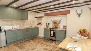 A kitchen with teal cabinets, a stone tile floor, a stove, and a wall-mounted deer head. - The La'al Cragg (Kirkby Stephen)