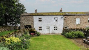 A stone house with a white exterior, a front door, and a small front yard with a lawn and garden. - The La'al Cragg (Kirkby Stephen)