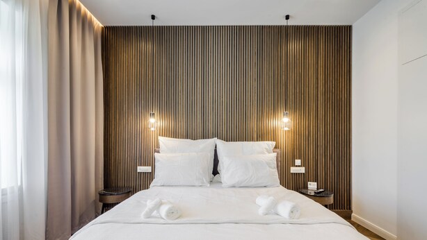 Een hotelkamer met een groot bed, twee nachtkastjes en een wand van houten latten.