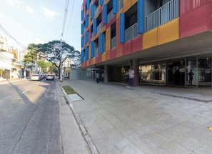Un edificio de varios pisos con fachada colorida, una acera y una calle con coches estacionados.