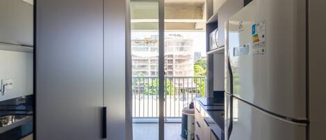 Une cuisine moderne équipée d’un réfrigérateur, de placards et d’une porte-fenêtre coulissante donnant sur un balcon.