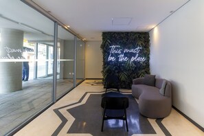 A modern interior with a glass wall, a neon sign, a green wall, and a sectional sofa. - 360 On Imarés by Housi (São Paulo)