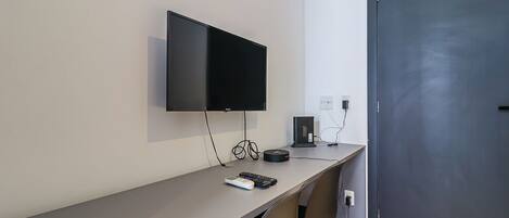 Una habitación de hotel moderna con un televisor de pantalla plana montado en la pared, un escritorio con una computadora y un control remoto, y una puerta con manija.