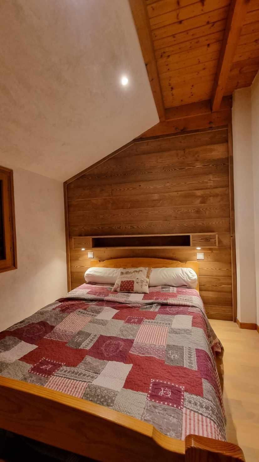 A bedroom with a wooden sloped ceiling, a bed with a quilt, and a nightstand.