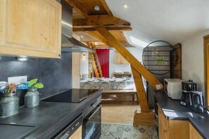 A modern kitchen with a black countertop, wooden beams, and a dining area with a red curtain.