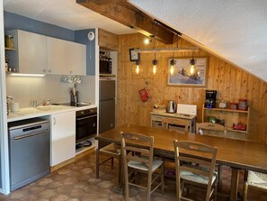 A compact kitchen with a wooden ceiling, a dining table with four chairs, and a built-in oven.