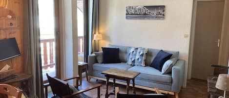 Una sala de estar acogedora con un sofá, dos sillas de madera, una mesa de centro y un televisor.