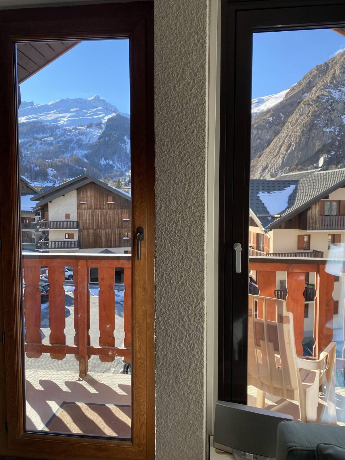 A wooden door with a view of snow-covered mountains and a wooden building with a balcony.