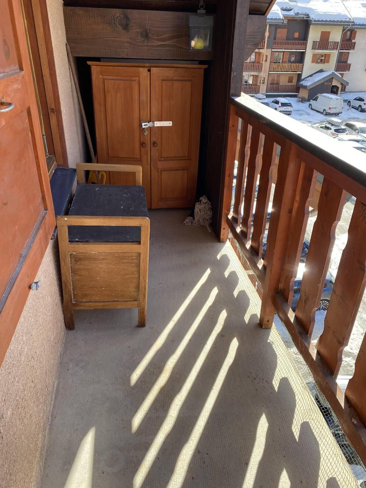 Un balcon avec un banc en bois, une petite table et une vue sur un paysage enneigé parsemé de bâtiments.