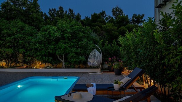 A pool area with lounge chairs and a hanging chair, surrounded by trees and potted plants. - Luxury Villa Essencia Milna Brac with Heated Pool (Milna (Brac))
