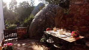 An outdoor dining area with a stone wall, a large rock, and a table set for two with chairs.