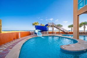 A swimming pool with a water slide, a staircase, and a view of the beach.