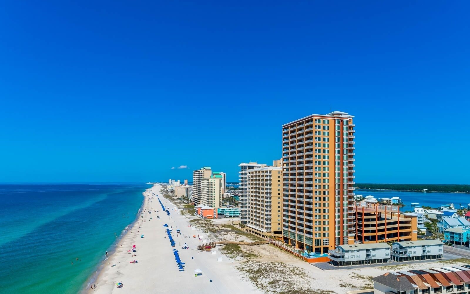 A coastal hotel with multiple high-rise buildings, a beach with umbrellas, and a clear blue sky.
