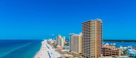 A coastal hotel with multiple high-rise buildings, a beach with umbrellas, and a clear blue sky.