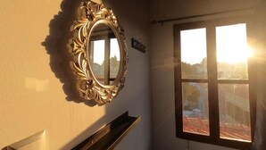 Een kamer met een grote, versierde spiegel aan de muur, een raam met uitzicht op een stadsgezicht en een plankje onder de spiegel.