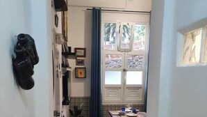 Un pasillo estrecho con suelo de madera, un comedor con mesa y sillas, una planta en maceta y un ventilador de techo.