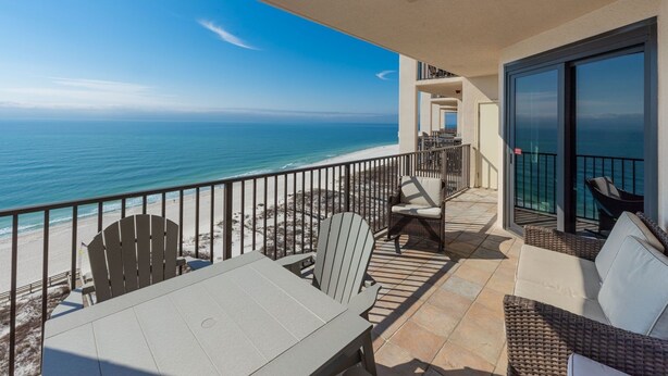 A balcony with a view of the ocean, outdoor seating, and a glass door. - Phoenix East 1406 3 Bedroom Condo (Orange Beach)