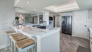 Une cuisine moderne dotée d’un îlot central, de meubles blancs, d’appareils électroménagers en acier inoxydable et d’un plancher en bois clair.