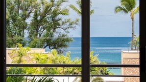 A balcony with a view of the ocean, surrounded by trees and palm plants.