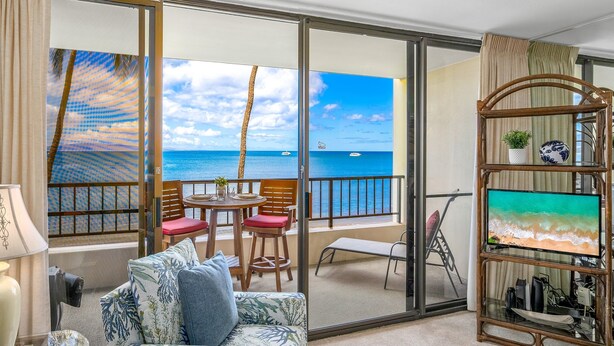 A room with a balcony, a sofa, a TV stand, and a view of the ocean.