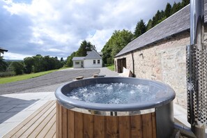 A hot tub in a rustic outdoor setting with a stone building and a grassy field in the background.