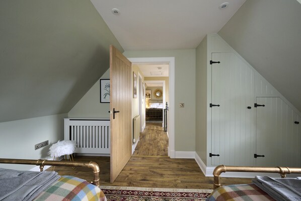 A bedroom with a wooden floor, a radiator, a fluffy white chair, and a bed with a checkered blanket.