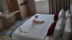 A hotel room with a neatly made bed, a dresser, and a window with curtains.