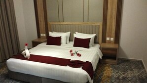 A hotel room with a large bed, wooden headboard, and a red accent on the bedspread.