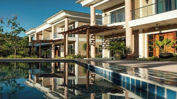 A modern hotel with a swimming pool, outdoor seating, and lush greenery. - Chez soi Loin de Chez soi (Anse Royale)