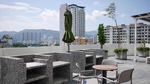 A rooftop terrace with outdoor seating, a green umbrella, and a view of a cityscape with buildings and mountains in the background.
